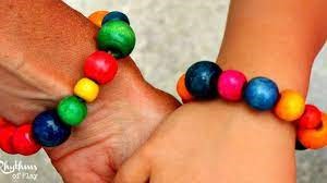 A picture of two white hands wearing colorful large bead bracelets. The people are holding hands. The beads appear to be made of wood. 