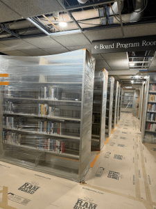 Image of the Adult nonfiction stacks wrapped in plastic, with the floor covered in protective boards. Parts of the ceiling have been removed