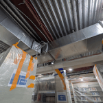 A photo of the ceiling with very shiny metal ductwork visible. 
